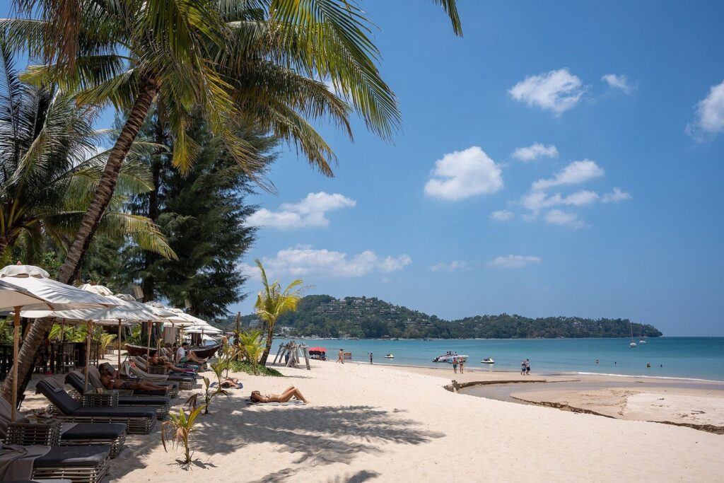 Two-Up Touring on the Honda PCX 160: Real Routes for Couples in Phuket 4 Sun loungers and umbrellas on Bang Tao Beach on Phuket's west coast with a headland in the distance