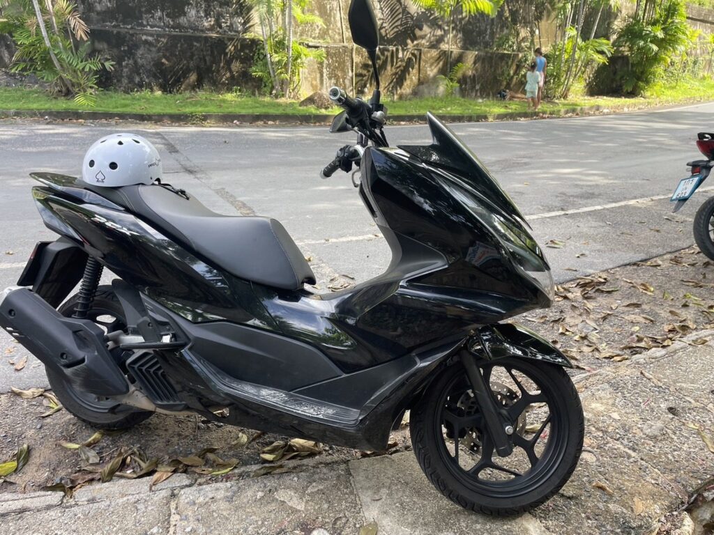 Motorbike Rental at Kata Noi 4 Black Honda PCX 160 scooter with a helmet on the seat beside a hillside road in Kata