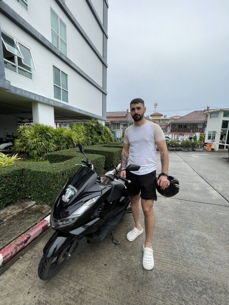 Motorbike Rental in Phuket Old Town 7 Customer holding a helmet beside a black Honda scooter outside a hotel in Phuket Town