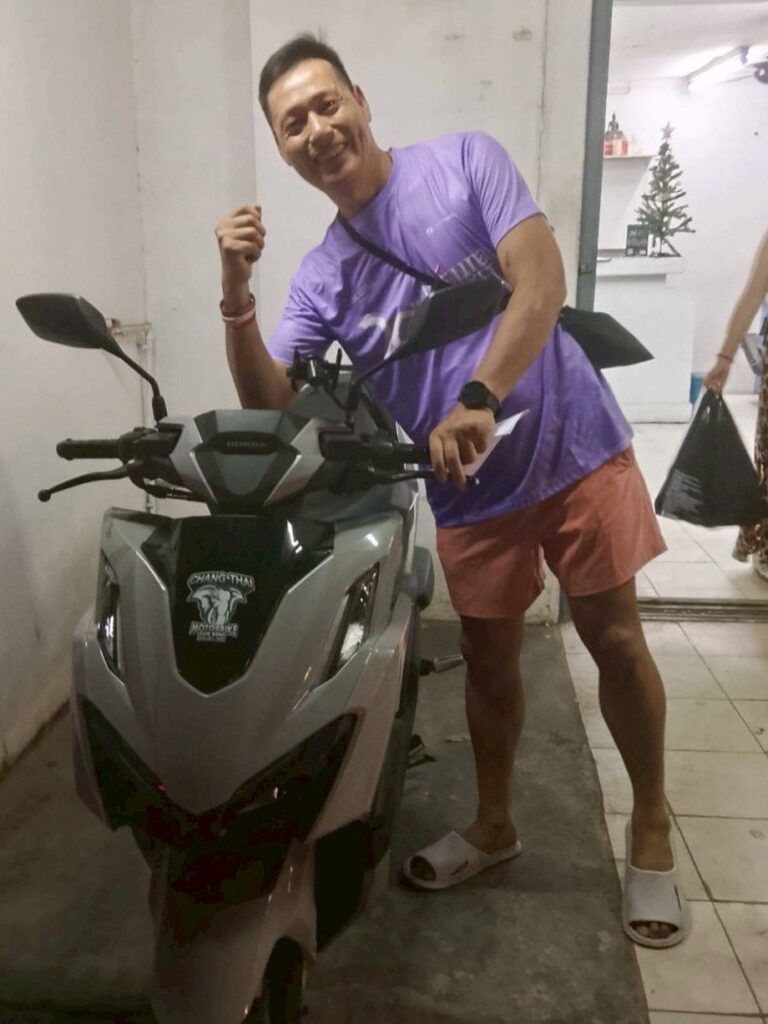 Motorbike Rental at Laguna Phuket 3 Smiling customer holding the handlebar of a grey Honda scooter with the Chang Thai elephant logo