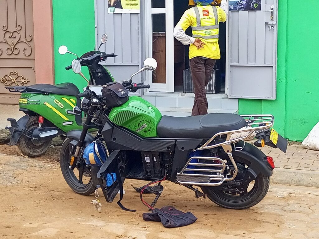 Electric Scooter Rental Phuket 2026 — What's Available, Honest Pros & Cons 5 Electric motorcycle parked beside a recharge point with a rider in a yellow vest