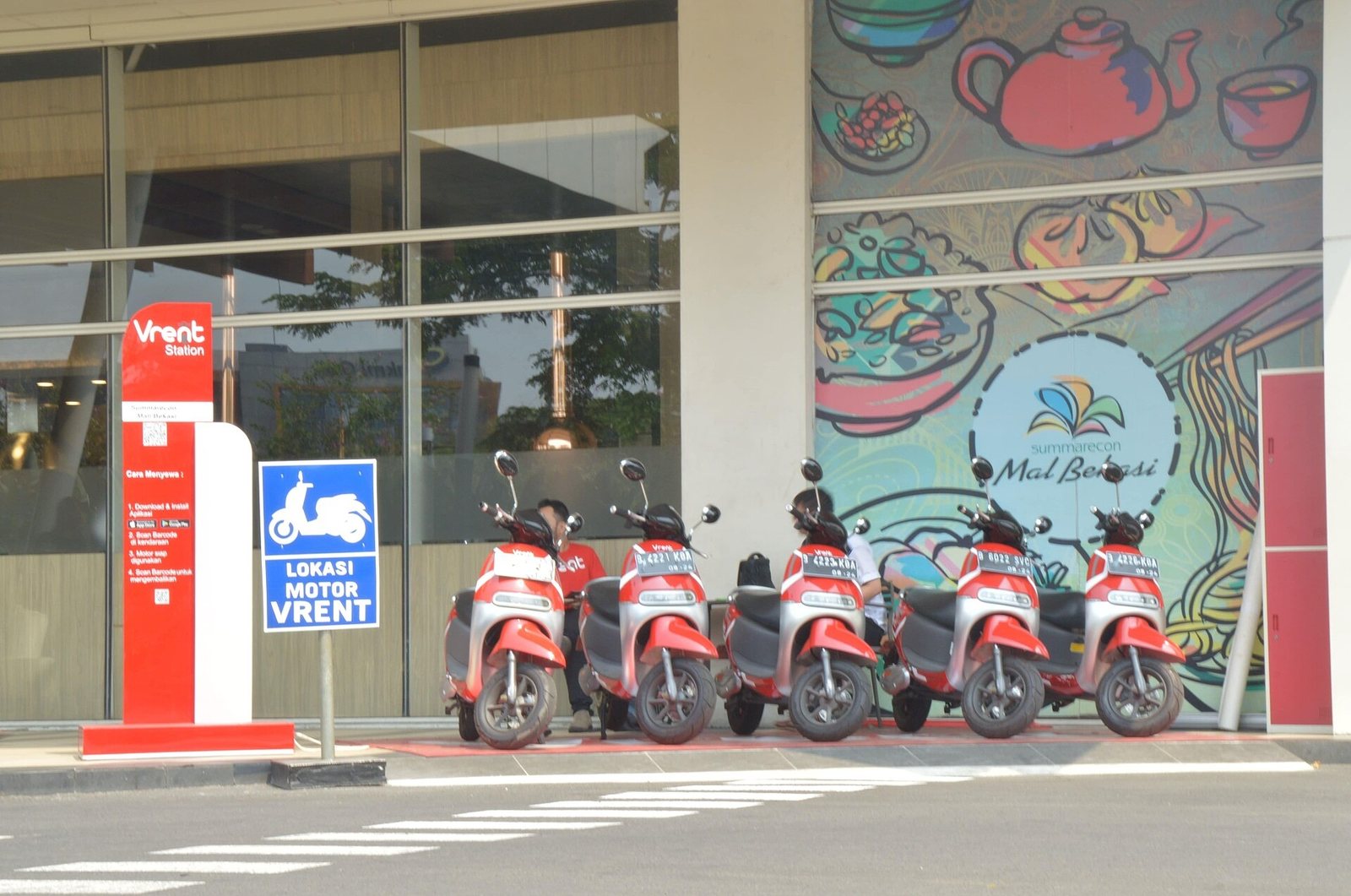 Row of electric scooters lined up at a rental point beside a mall entrance