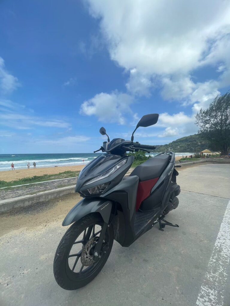 Motorbike Rental at Karon Beach 2 Dark Honda Click 160 scooter parked on the road beside Karon Beach with the sea behind