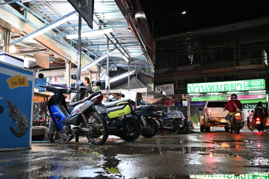 Wet street at night after rain with motorbikes parked outside shops in Thailand