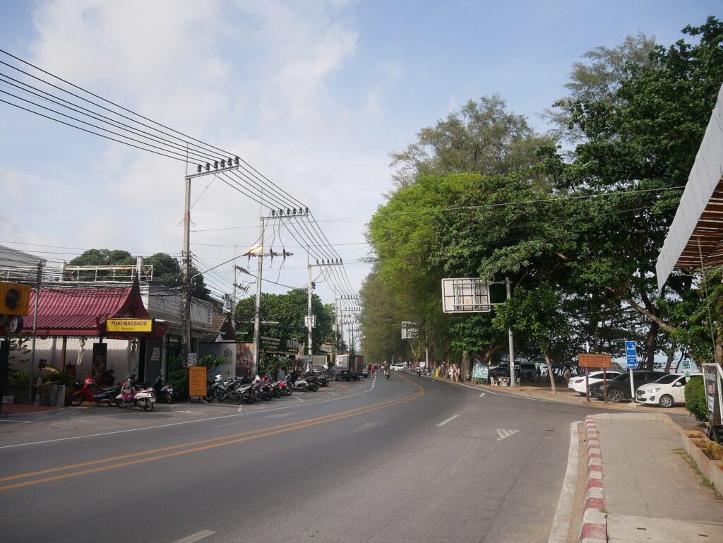 Phuket Scooter Route: Big Buddha, Promthep Cape & Rawai — Half-Day Guide 2026 5 Road through Rawai in Phuket with scooters parked under trees beside the road