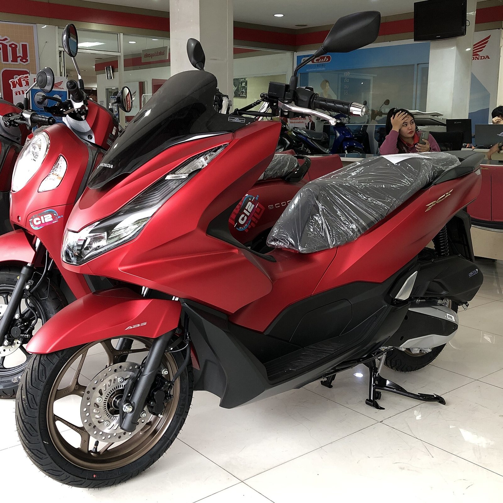 Red Honda PCX 160 ABS scooter on a dealer showroom floor