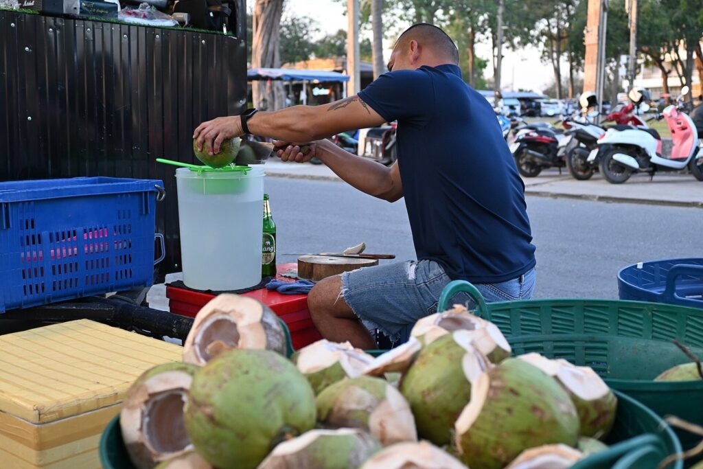 Heatstroke When Riding a Motorbike in Phuket: Warning Signs, First Aid, and Prevention 1 Street vendor preparing fresh coconuts at a roadside stall in Thailand