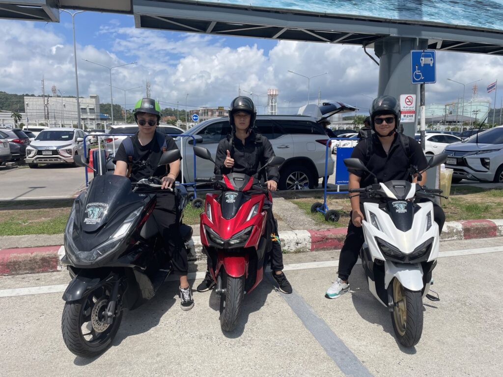 Motorbike Rental at Phuket International Airport 7 Three riders in helmets on black, red and white rental scooters outside Phuket Airport
