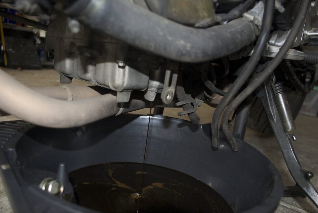 How to change engine oil level for Honda pcx160 2023 by myself? 2 Used engine oil draining from a motorcycle engine into a drain pan during an oil change